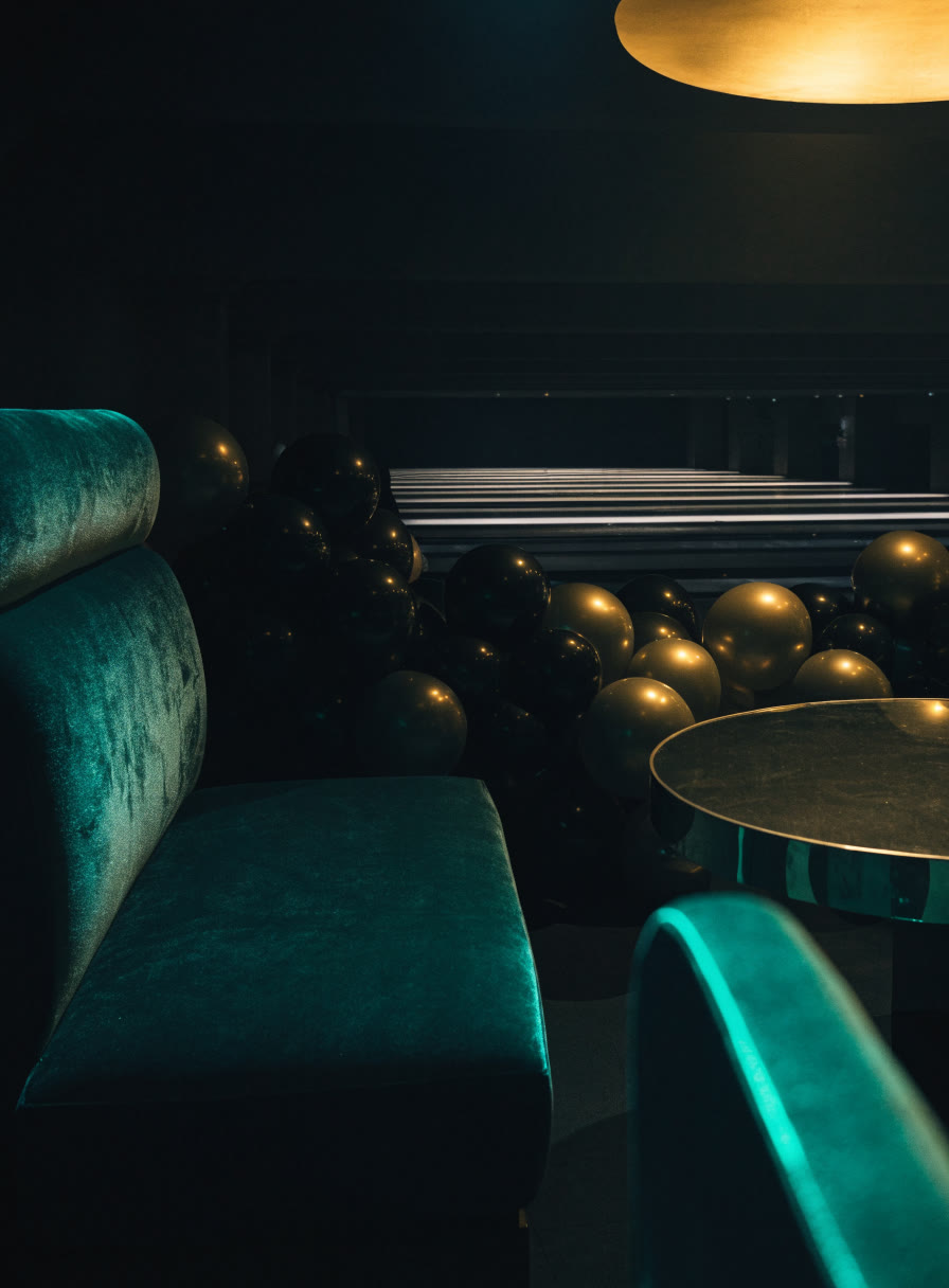 Rincón de eventos con globos dorados y un sillón de terciopelo