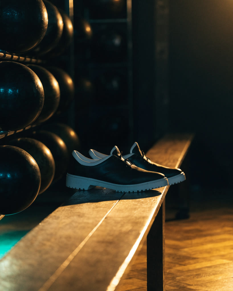 Zapatos de boliche sobre una banca junto al rack de bolas