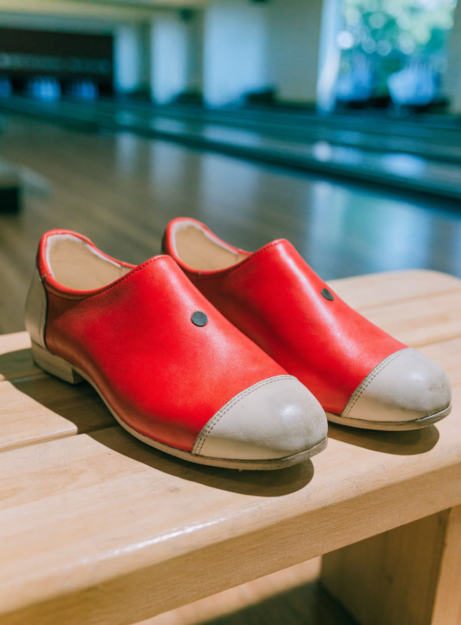 Zapatos de boliche rojo y crema sobre una banca de madera