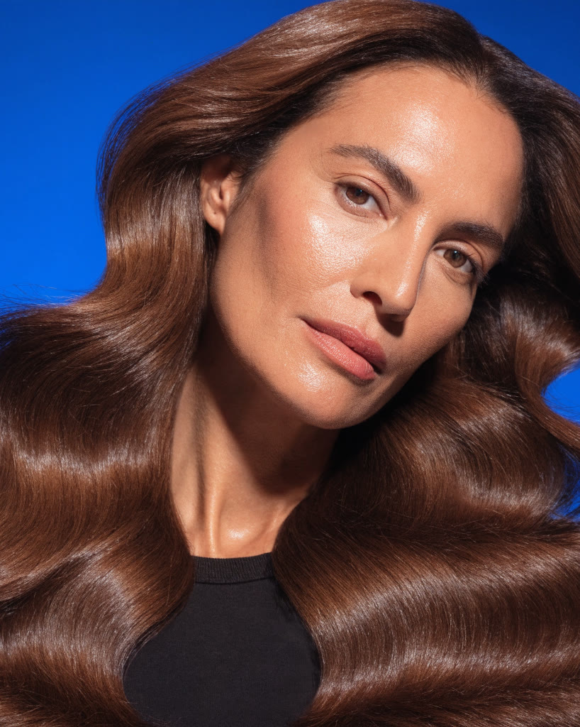 Mujer con cabello largo castaño en ondas sobre fondo azul