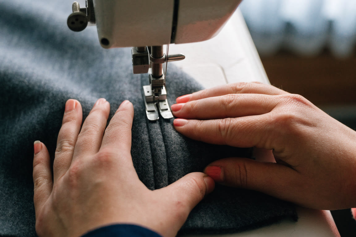 Manos trabajando una costura sobre tela en una mesa de taller