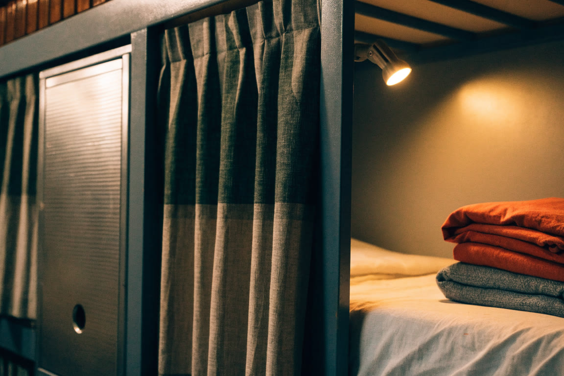 Detalle de cama de hostal con cortina y luz de lectura