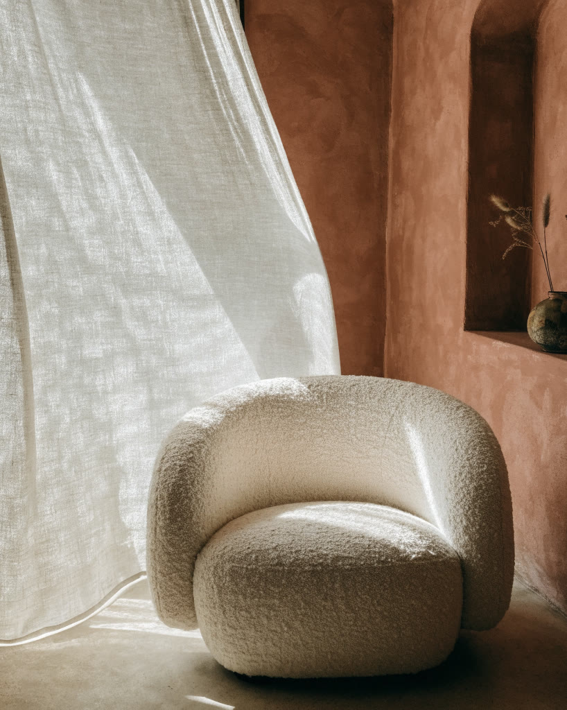 Sillón curvo junto a una cortina de lino con luz de día