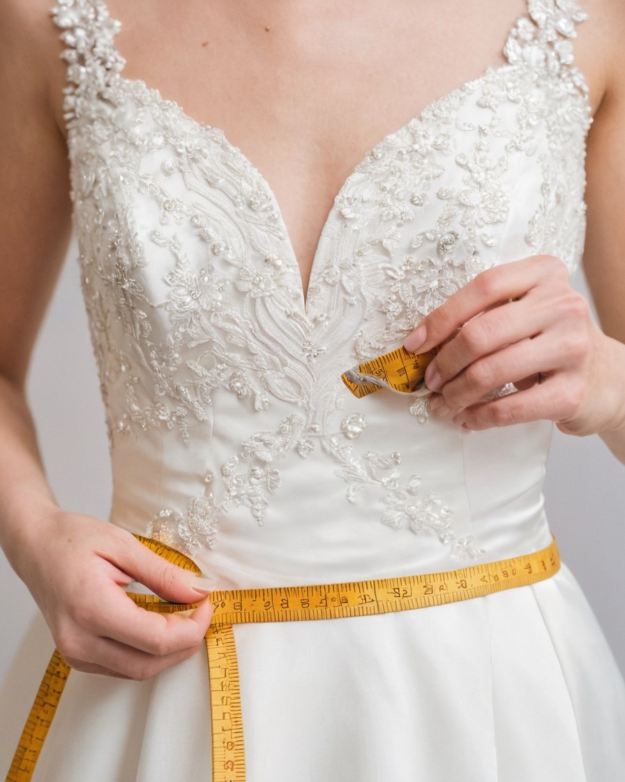 Costurera mide la cintura de un vestido de novia marfil con una cinta ocre