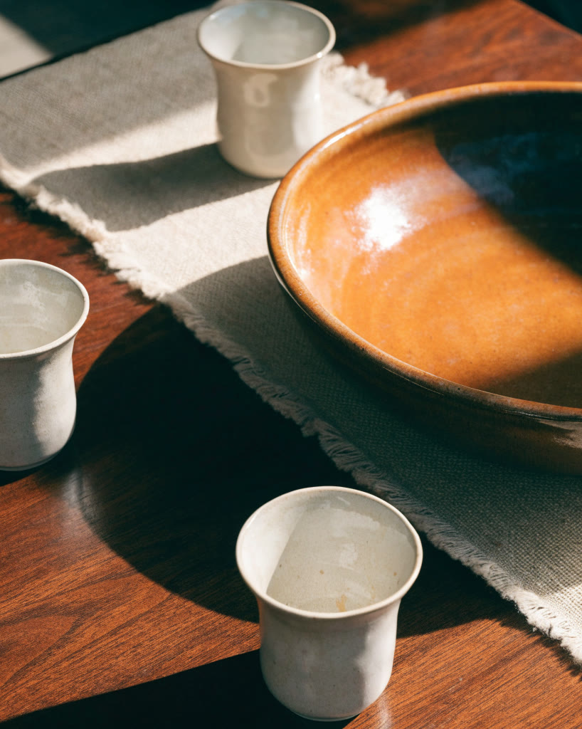 Tazón de barro esmaltado y tazas sobre mesa de nogal