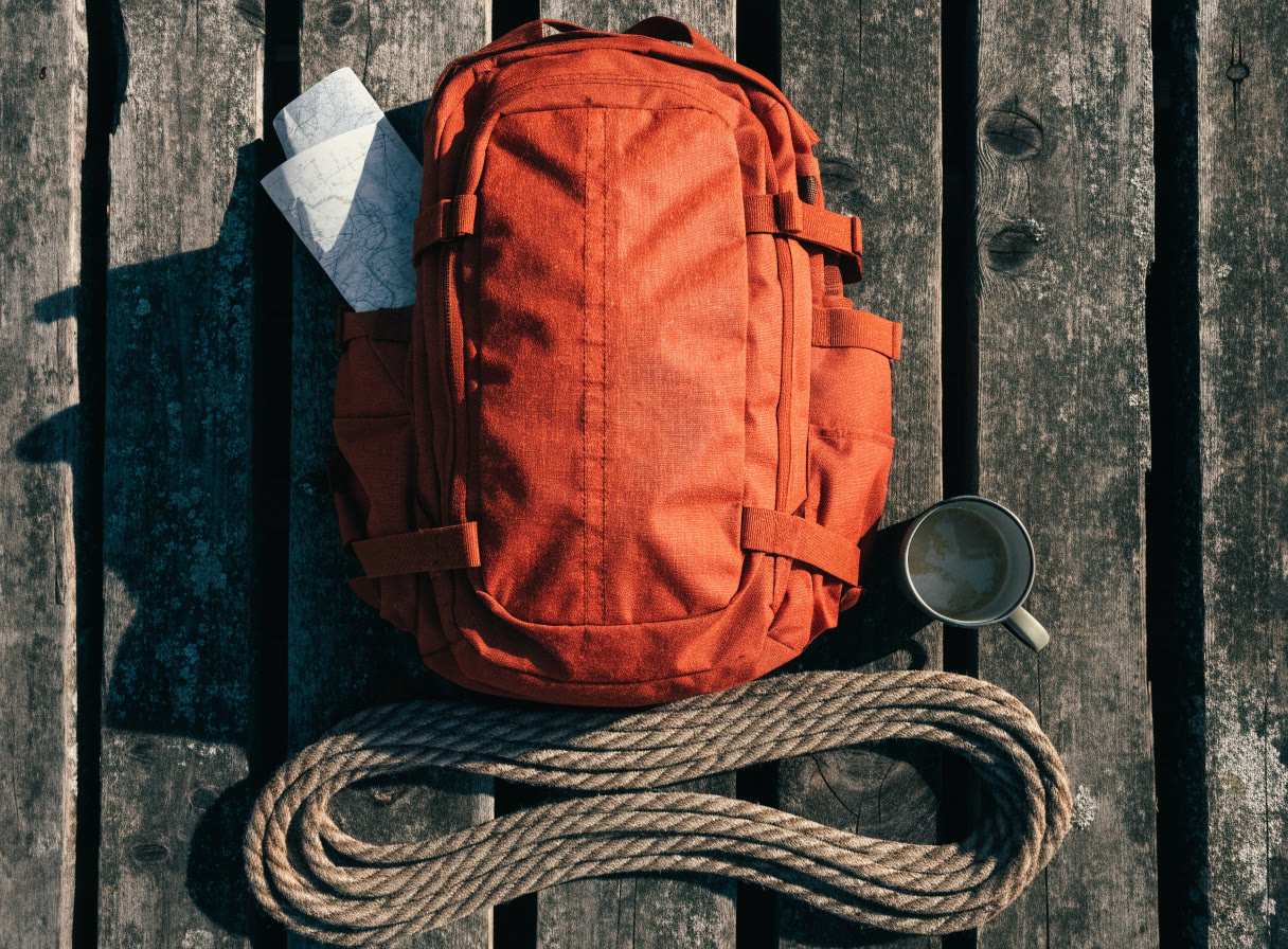 Mochila naranja, mapa doblado, taza de metal y cuerda sobre madera